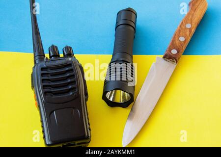 Equipment for trekking. Set of traveler or tourist or soldier. Radio for communication, knife, flashlight on a blue and yellow background. Stock Photo
