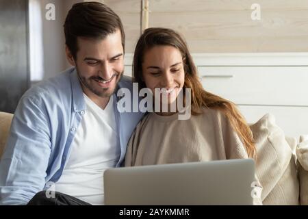Smiling millennial couple relax on couch using laptop Stock Photo