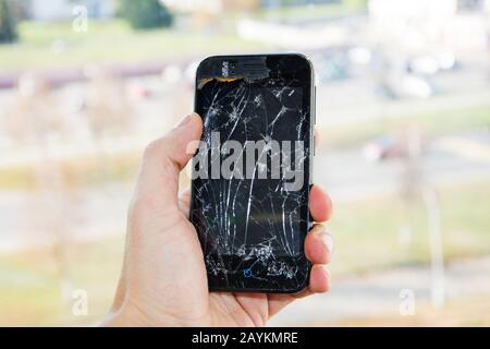 Broken glass screen smartphone in hand of upset man. The guy is holding a black smartphone with a broken display. Broken screen of modern gadget. a la Stock Photo
