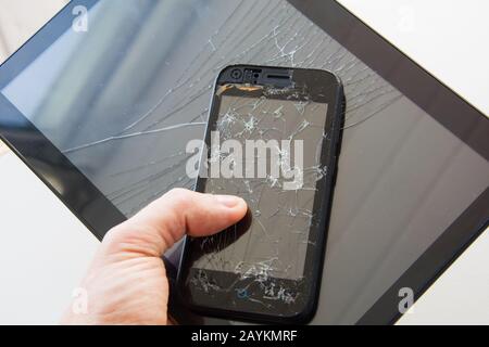 Broken glass screen smartphone in hand of upset man. The guy is holding a black smartphone with a broken display. Broken screen of modern gadget. a la Stock Photo