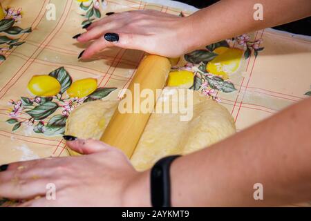 A housewife girl prepares dough from flour, water and yeast for the pizza base. Rolls it with a rolling pin, making the layer of dough as thin as poss Stock Photo