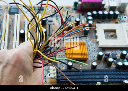 A man holds in his hand a harness of different colors on the background of the motherboard of the computer. Concept of repair of faulty computer equip Stock Photo