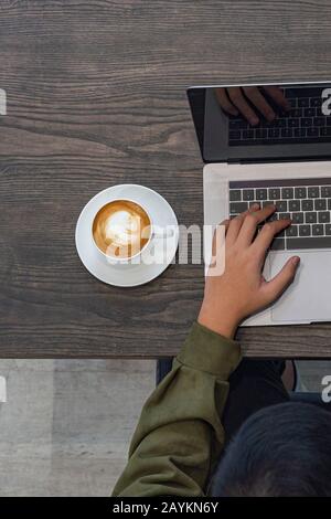 Top view of freelancer in mid green hoodie typing on laptop Stock Photo