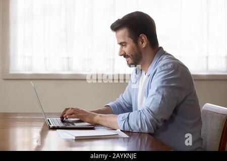 Smiling man using modern laptop typing message Stock Photo