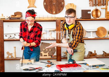 A man and a woman work together and have a good time in the carpentry shop. The concept of teamwork and manual labor Stock Photo
