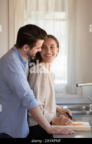 Loving newlyweds cuddle in kitchen cooking together Stock Photo