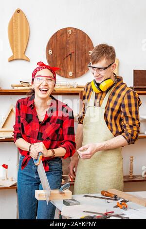 A man and a woman work together and have a good time in the carpentry shop. The concept of teamwork and manual labor Stock Photo