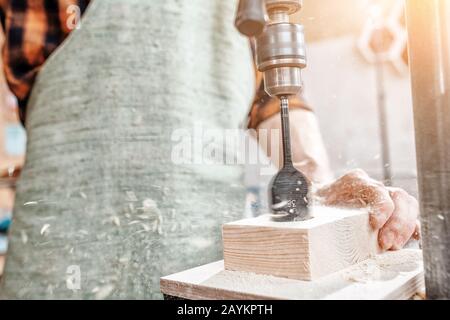 Close-up of a joiner hands working with wood on a lathe drilling machine at the factory. Carpenter equipment concept Stock Photo