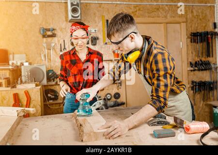 man and woman as a team working in the workshop with wood and polishing it with mechanical tools Stock Photo