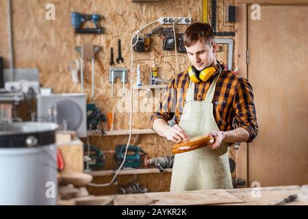 Happy talented caucasian carpenter working with wood in workshop, art and creativity concept Stock Photo