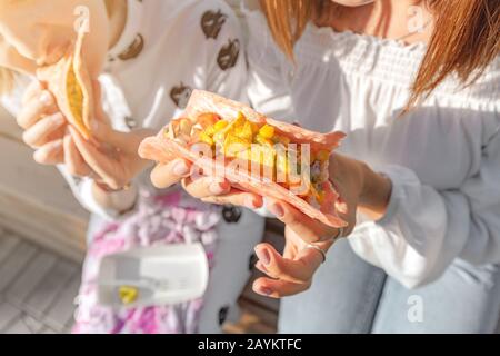 Two girls eat traditional Mexican fast food tacos and drink michelada on the street. Communication and takeaway food concept Stock Photo