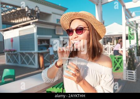 Happy asian woman drinking fresh detox lemonade with cucumber slices in outdoors cafe at city street Stock Photo