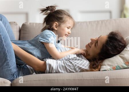 Smiling cute preschool daughter lying on cheerful mommy. Stock Photo