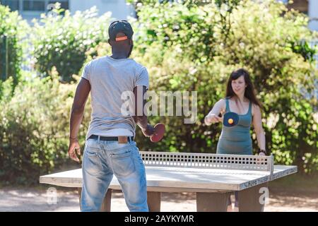 22 MAY 2018, LEIPZIG, GERMANY: multiracial couple playing ping pong table tennis outdoors Stock Photo