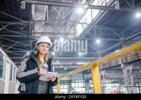 Young female technician in uniform, protective eyeglasses and helmet. Production workshop Stock Photo