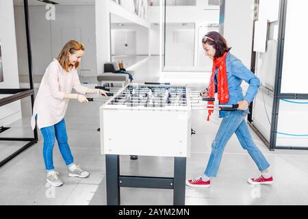 Two girls friends playing table football mini game indoors Stock Photo