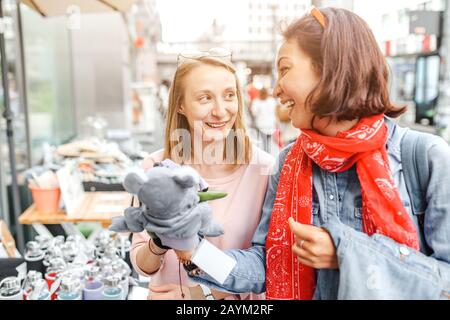 Young pretty hipster girls friends having fun outdoor on the street. Shopping together for cute souvenirs and toys Stock Photo