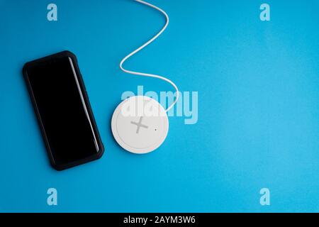 Smartphone charging on a charging pad or dock on blue background. Wireless charging Stock Photo
