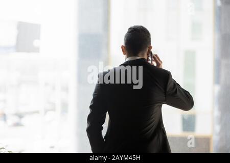 Rear view businessman in formal suit talking on phone indoors Stock Photo