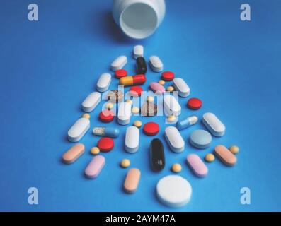 Colorful pills pouring out of white bottle on blue background. Pharmacy and medicine concept. Stock Photo