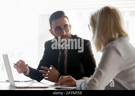 Diverse business partners seated at desk talking negotiating together Stock Photo