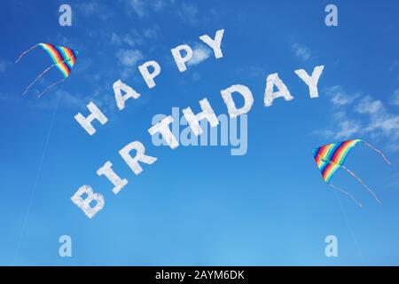 Happy birthday sign text made of clouds letters over clear day blue sky with colorful flying kites Stock Photo