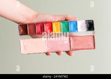 Female hand holds a palette with paints. Drawing or creating makeup. Theatrical makeup. Training in drawing, art school Stock Photo