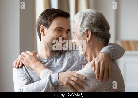 Excited middle aged hoary father cuddling grownup son. Stock Photo