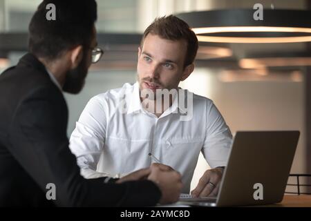 European and arabian male colleagues talking seated at office desk Stock Photo