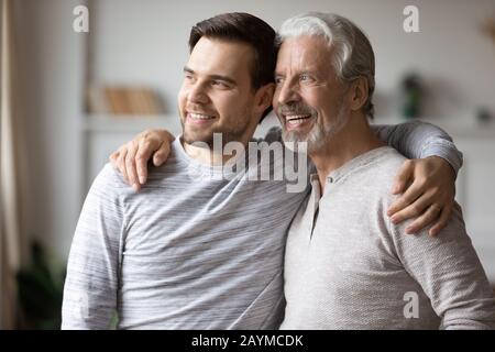 Grownup son embracing shoulders of happy middle aged father. Stock Photo