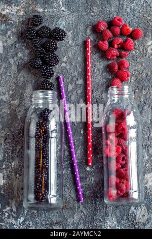 Blackberry and raspberry fruit in glass bottles with straws on stone background. Fresh organic Smoothie ingredients. Superfoods and health or detox diet food concept.