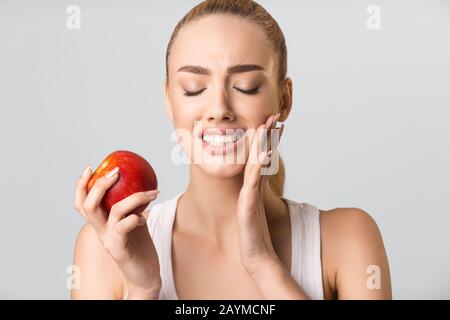 Young Woman Having Tooth Pain Eating Apple On Gray Background Stock Photo