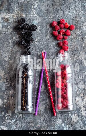 Blackberry and raspberry fruit in glass bottles with straws on stone background. Fresh organic Smoothie ingredients. Superfoods and health or detox diet food concept. Stock Photo