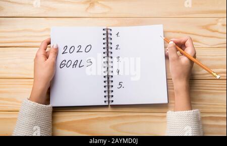 Female planning 2020 goals list in notebook on wooden table Stock Photo