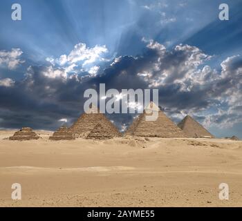 Sun shines from clouds above the Giza pyramid complex or the Giza Necropolis on the Giza Plateau in Egypt near Cairo includes the Great Pyramid of Giz Stock Photo