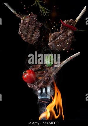 food photography of bbq rack of lamb on fire with spices and vegetables on black background Stock Photo