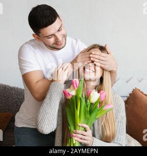 Man gifting his wife tulips flowers and covered her eyes Stock Photo