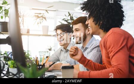 Three guys colleagues looking at laptop screen, celebrating success Stock Photo