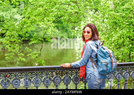 young pretty brunette woman traveling in park and standing on a bridge over old channel Stock Photo