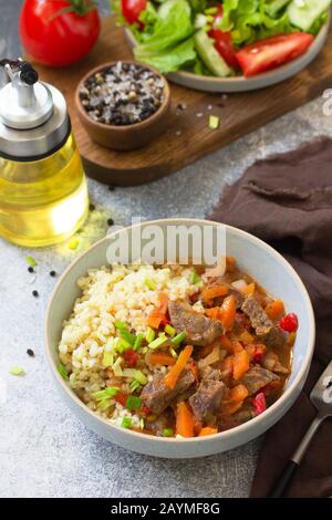 Healthy eating concept. Beef stewed with vegetables in bulgur sauce and fresh vegetable salad on a light stone table top. Stock Photo