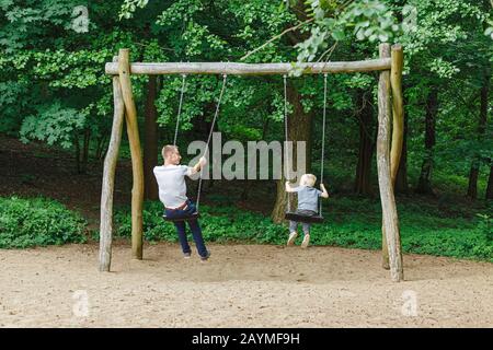 16 MAY 2018, BERLIN, GERMANY: Father And Son Having Fun On Swing In Playground in park Stock Photo