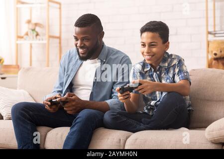 Excited Black Boy Playing Video Games With Dad At Home Stock Photo