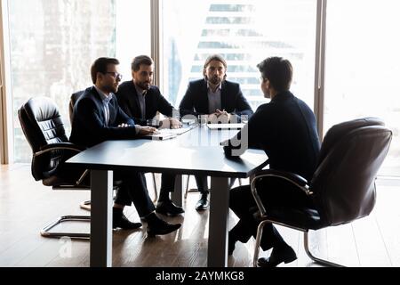 Applicant sitting in front three serious HR businessmen speaking. Stock Photo
