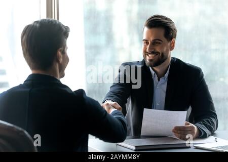 Smiling bearded businessman in suit shaking hands with job seeker. Stock Photo