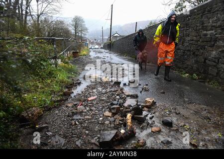 Trehorchy, Rhonnda Valley, UK 16th February 2020. UK Weather : Two people walk past debris above Dumfries Street in Trehorchy, Rhondda Valley, where locals and residents made their own flood defenses after a culvert brought water cascading into the street from the hill above. Credit: Robert Melen/Alamy Live News. Stock Photo