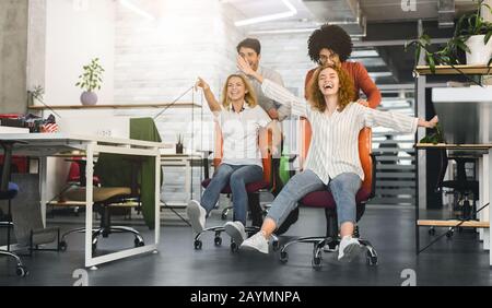 Carefree young colleagues having chair race competition in office Stock Photo