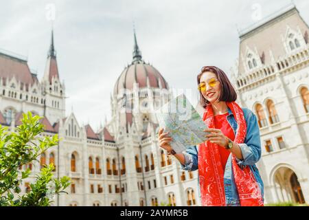 Happy asian hipster woman tourist with map travels in Budapest at Hungarian Parliament at the background Stock Photo