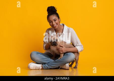 Beautiful Black Girl Posing With French Bulldog Puppy Over Yellow Background Stock Photo