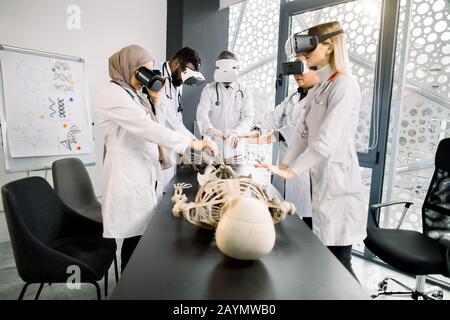 Education, science, vr, medical and health concept. Group of multiethnic doctors, biologists, archeologists, scientists wearing VR goggles study human Stock Photo