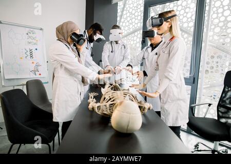 Young multiethnic doctors, bioengeneers, scientists with virtual reality equipment vr goggles in the laboratory working with human skeleton anatomy Stock Photo